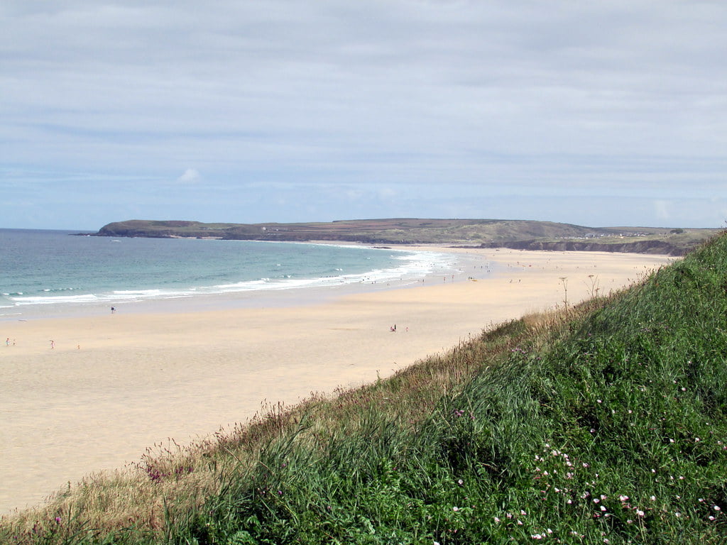 Hayles Towans Beach with a few people enjoying the sun and a few others strolling along the sandy shore.