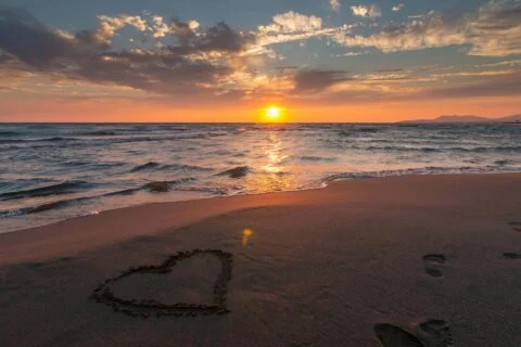 A heart drawn on sandy beach of Hayle Cornwall at sunset, symbolizing love and romance in a serene setting.
