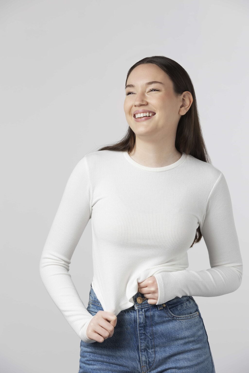 A stylish woman radiates joy with her bright smile in a casual white J.Crew Perfect Fit Long-Sleeve T-Shirt and jeans.