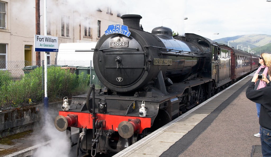 A Jacobite steam train arrives at the station, with excited onlookers eagerly watching its grand entrance.