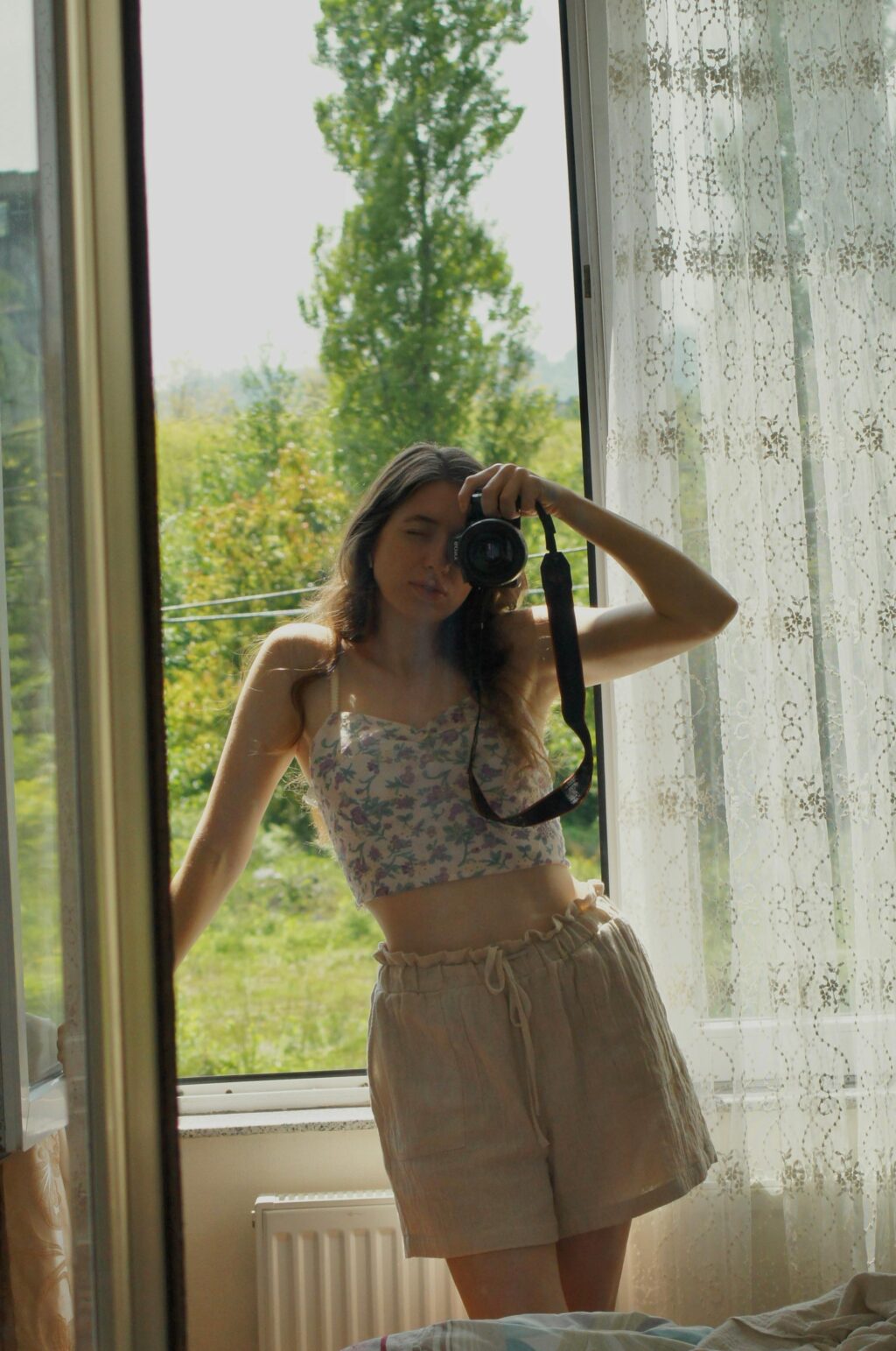 A woman capturing a self-portrait in front of a window, showcasing her style while wearing linen shorts