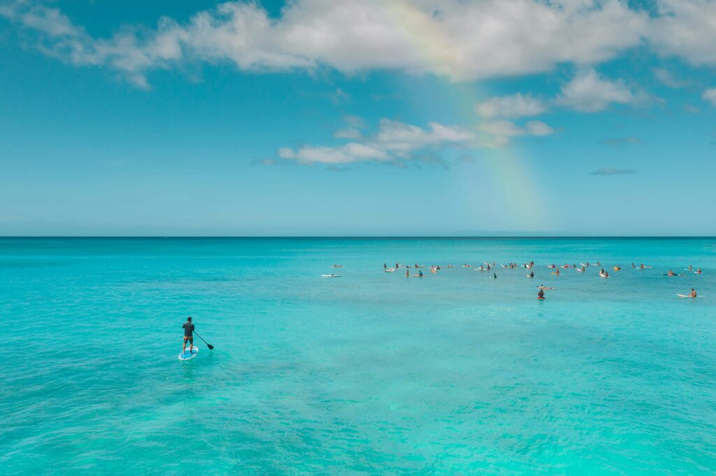 A picturesque rainbow beautify the sky, accompanied by people paddle boarding in the Atlantic ocean near the Beaches of Hayle Cornwall.