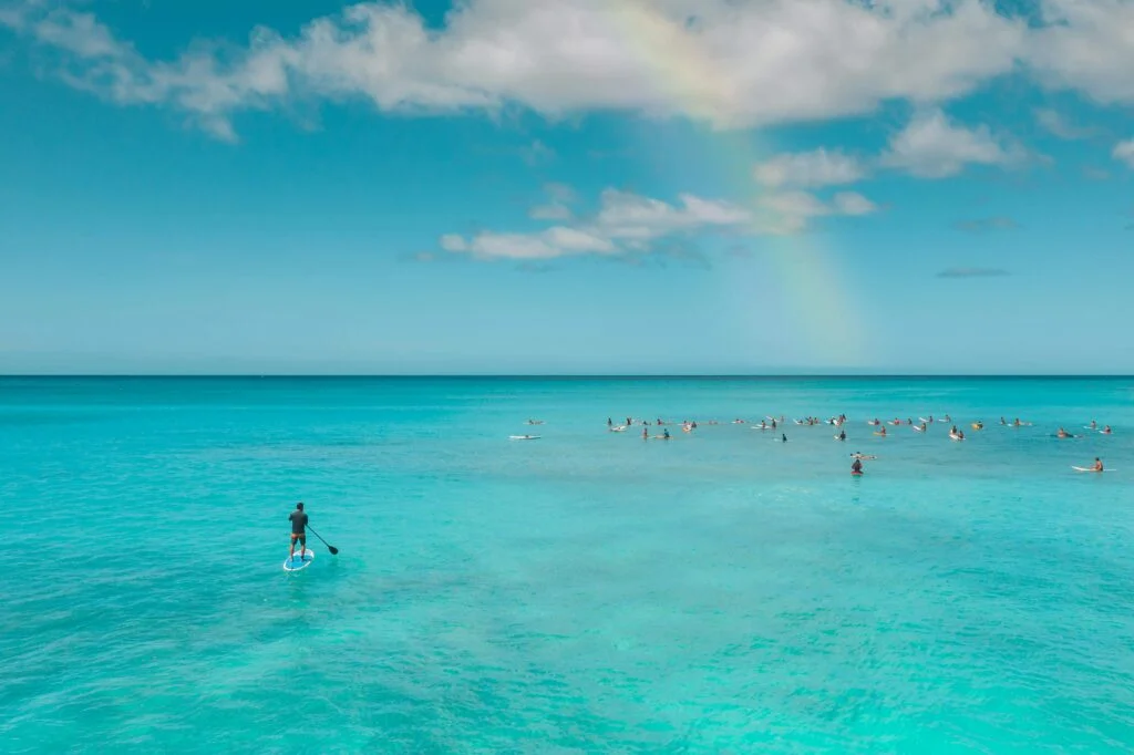 A picturesque rainbow beautify the sky, accompanied by people paddle boarding in the Atlantic ocean near the Beaches of Hayle Cornwall.