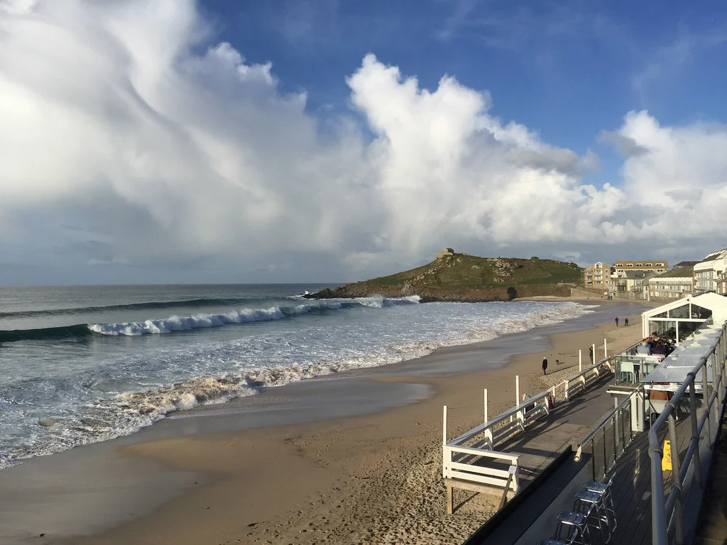 Porthmeor Beach in St Ives, where white clouds in the sky and waves are coming to the beach creating an mesmerizing view.