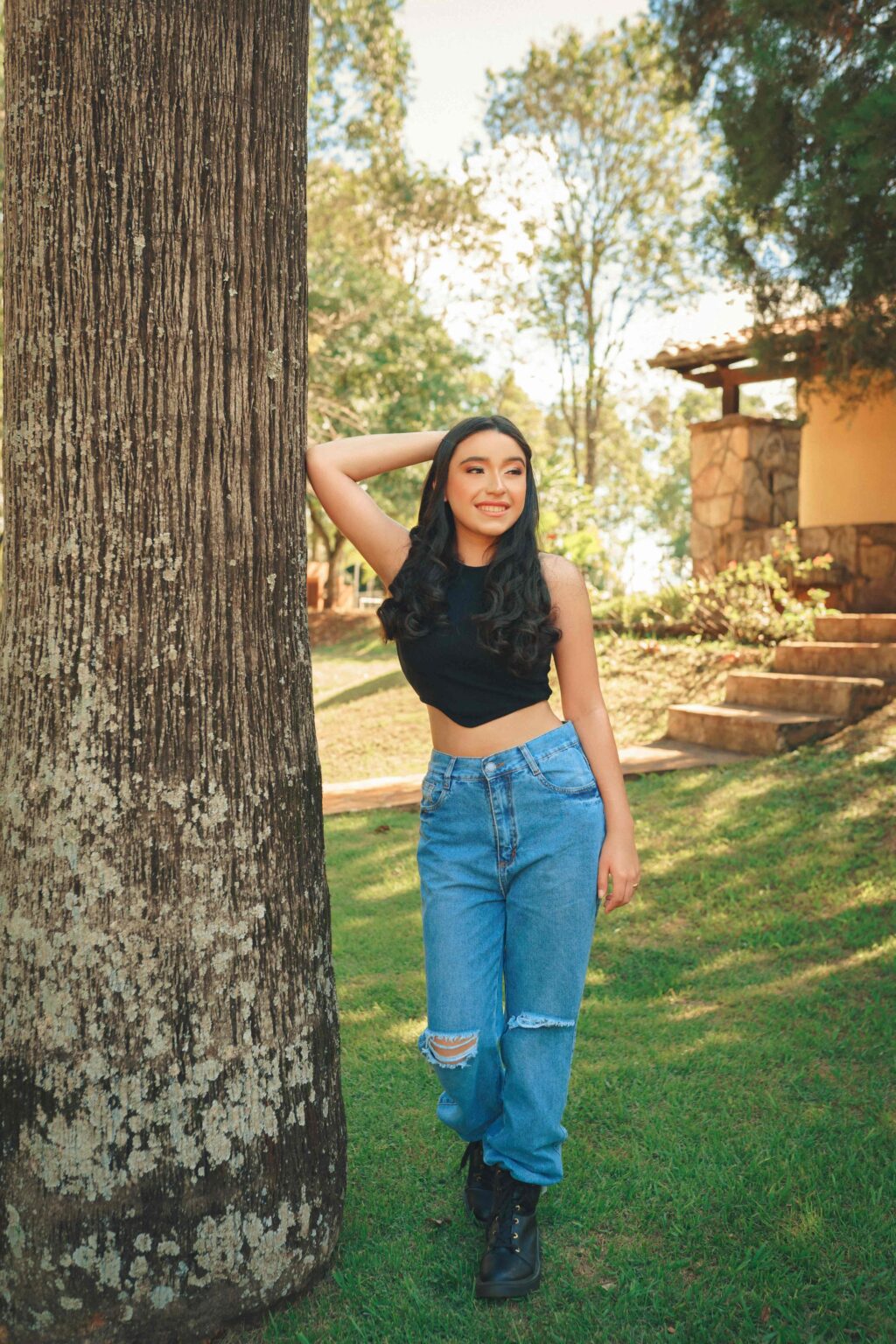 A stylish woman in Mid-Waisted Wide-Leg Jeans and a crop top, casually leaning against a tree, exuding confidence and cool vibes.