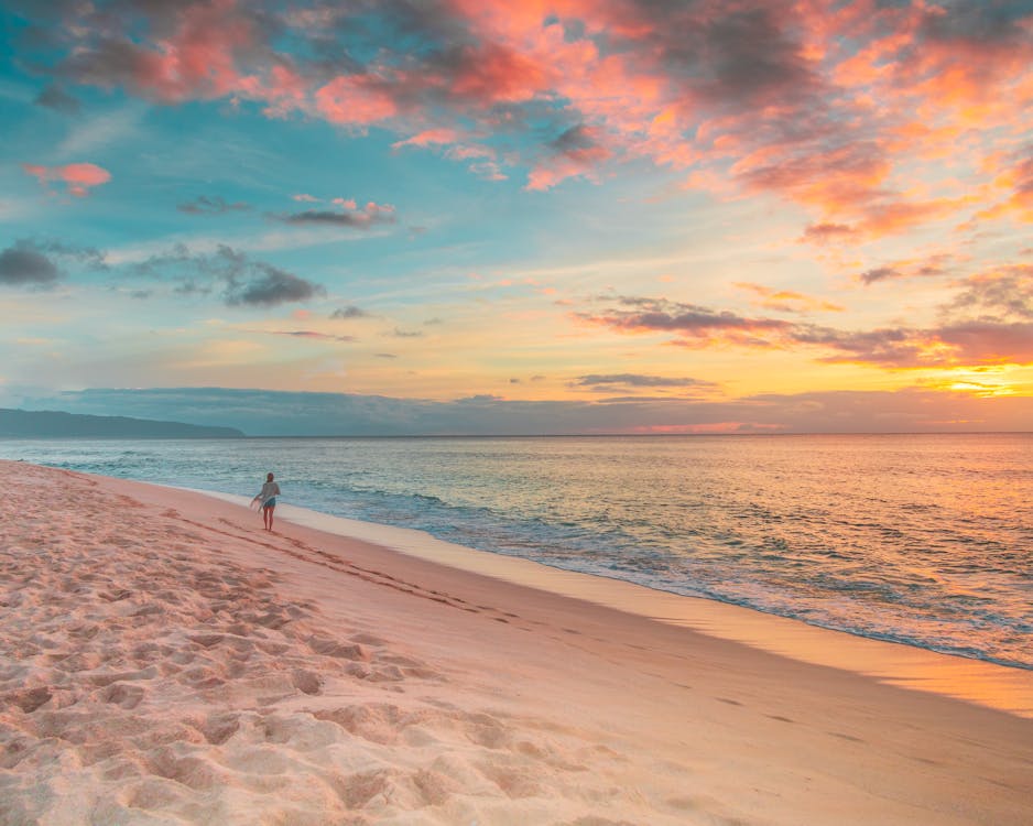 A person strolling on Oahu's Island beach at sunset.