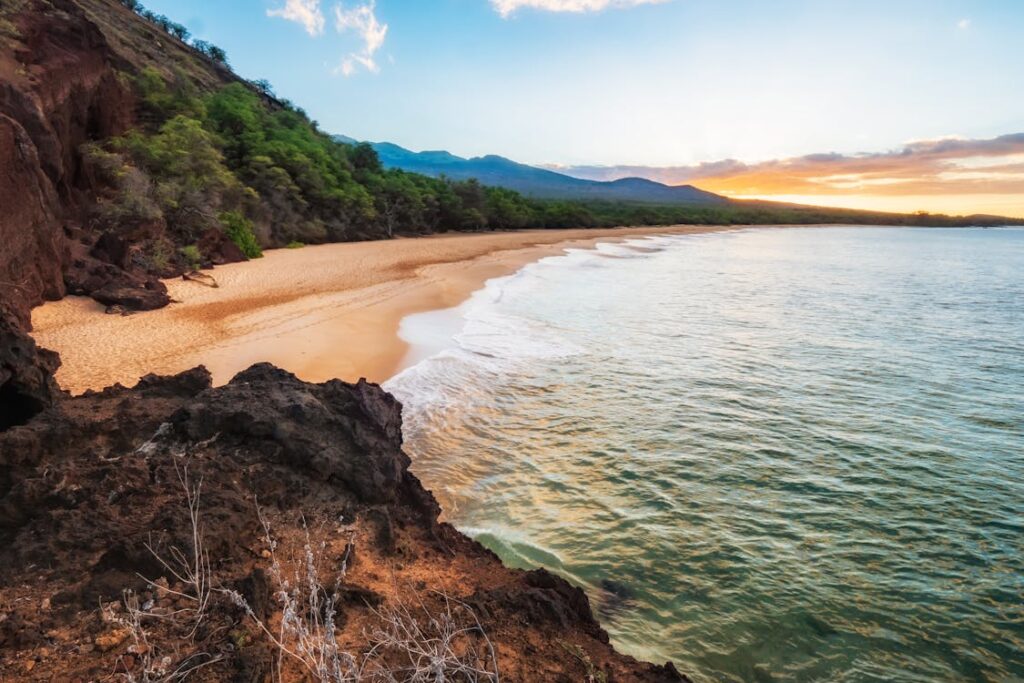 Gorgeous Maui Island sunset with mountains in the distance, casting a warm glow over the beach.
