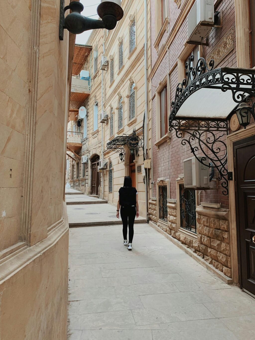 A visitor walks along a quaint narrow street in Bourton-on-the-Water, exploring the sights on the Bloody Bourton Walking Tour.