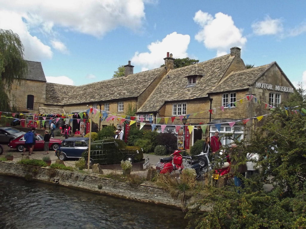 People enjoy the riverside while cars are parked outside the Cotswolds Motoring Museum in Bourton-on-the-Water.