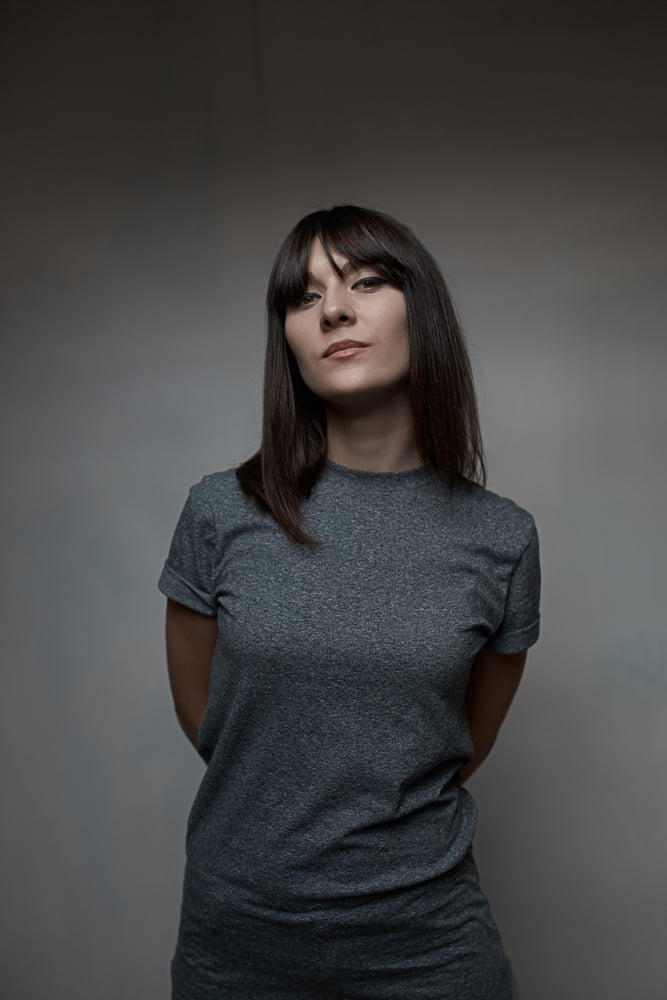 A woman in a gray crew neck t-shirt smiles and poses confidently for the camera, showcasing her stylish look.