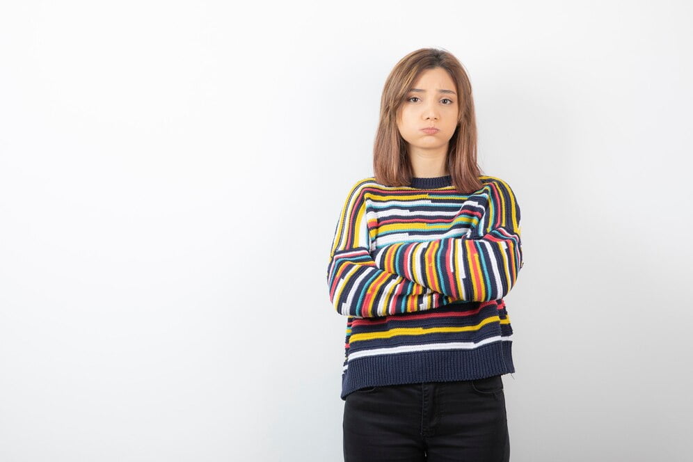 A woman in a striped sweater stands confidently with her arms crossed, showcasing her stylish ELEVEN cropped t-shirt.