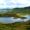 Snowdonia National Park landscape with two tranquil lakes linked by a slender pathway. The scene is enveloped by lush, green hills, with mountains visible in the background beneath a sky dotted with clouds.