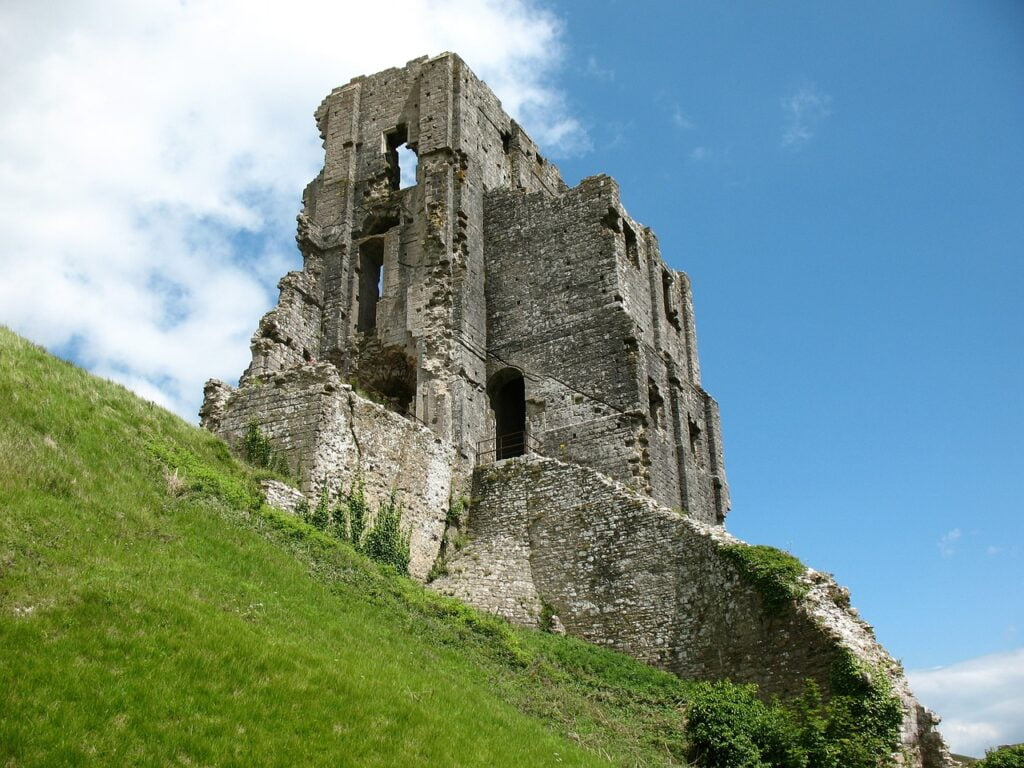 Corfe Castle stands majestically on a hillside, framed by verdant landscapes and a bright, sunny atmosphere.