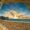 A breathtaking view of the Jurassic Coast at sunset, seen through a rocky archway framing the sandy beach, calm sea, and dramatic cliffs under a vibrant sky with golden clouds.