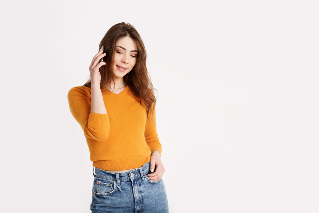 A woman in a yellow Gap Essential Long Sleeve Crewneck T-Shirt and jeans chatting on her phone with a smile.