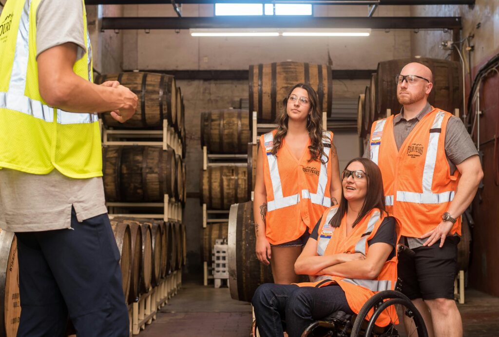 At Hawkstone Brewery in Bourton-on-the-Water, three people in safety vests and wheelchairs stand together in a warehouse.