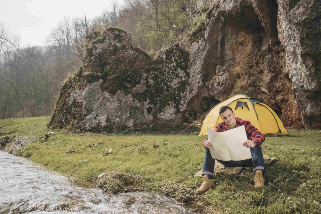 A man sits in front of a tent at Nantcol Waterfalls Campsite, studying a map in Snowdonia National Park.