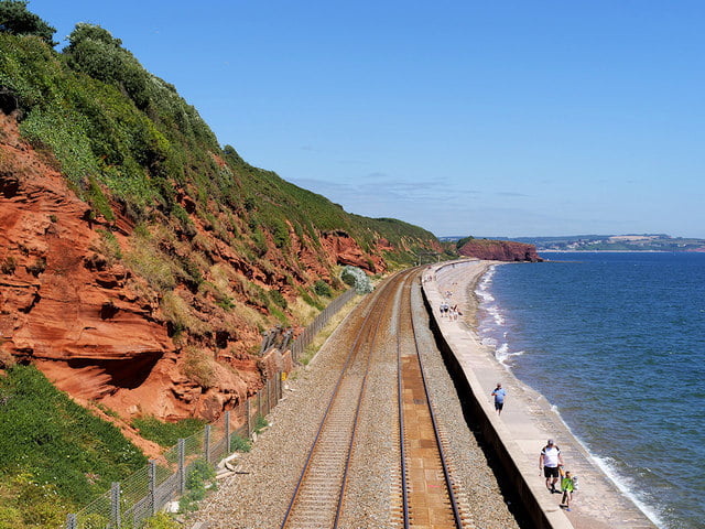 Scenic view of train tracks by Red Sandstone Cliffs in the East Devone beach with people walking.