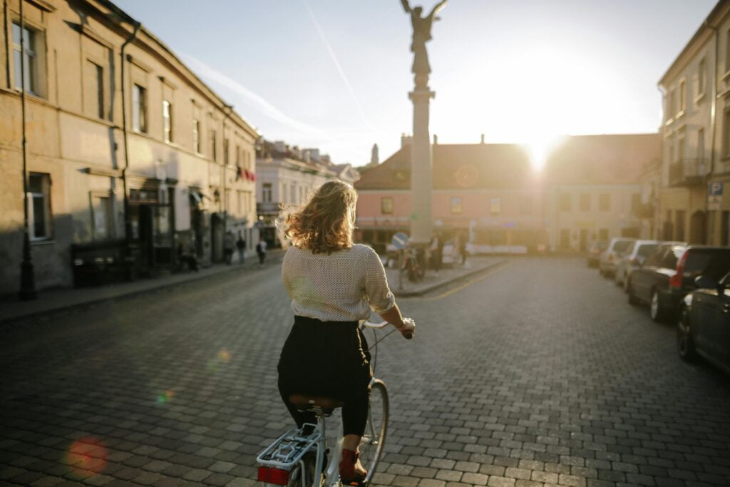 A woman joyfully rides her bicycle along a picturesque street in Bourton-on-the-Water, surrounded by charming scenery.