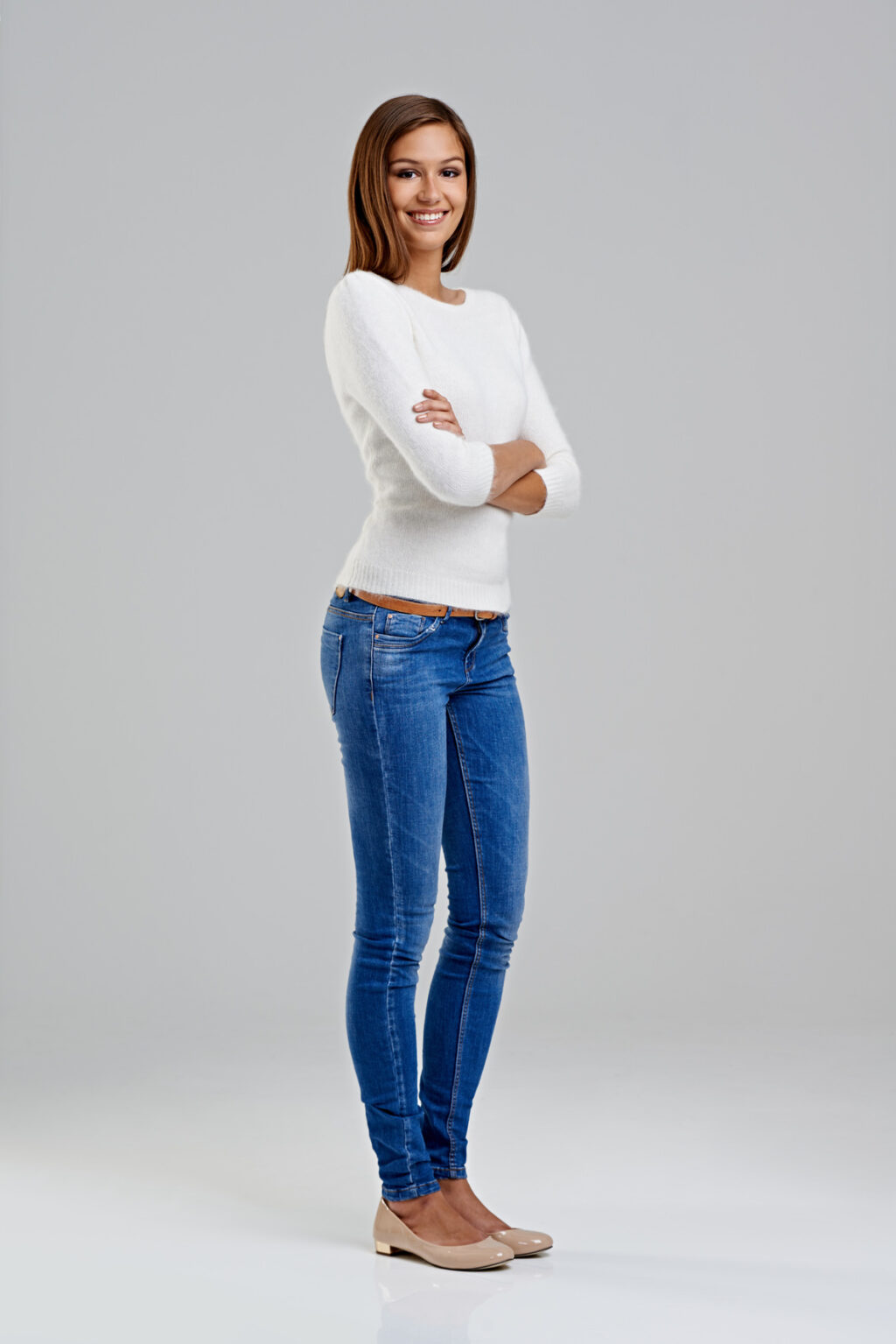 A young woman wearing skinny jeans and a white shirt, paired with lightweight flats, stands confidently in a casual pose.