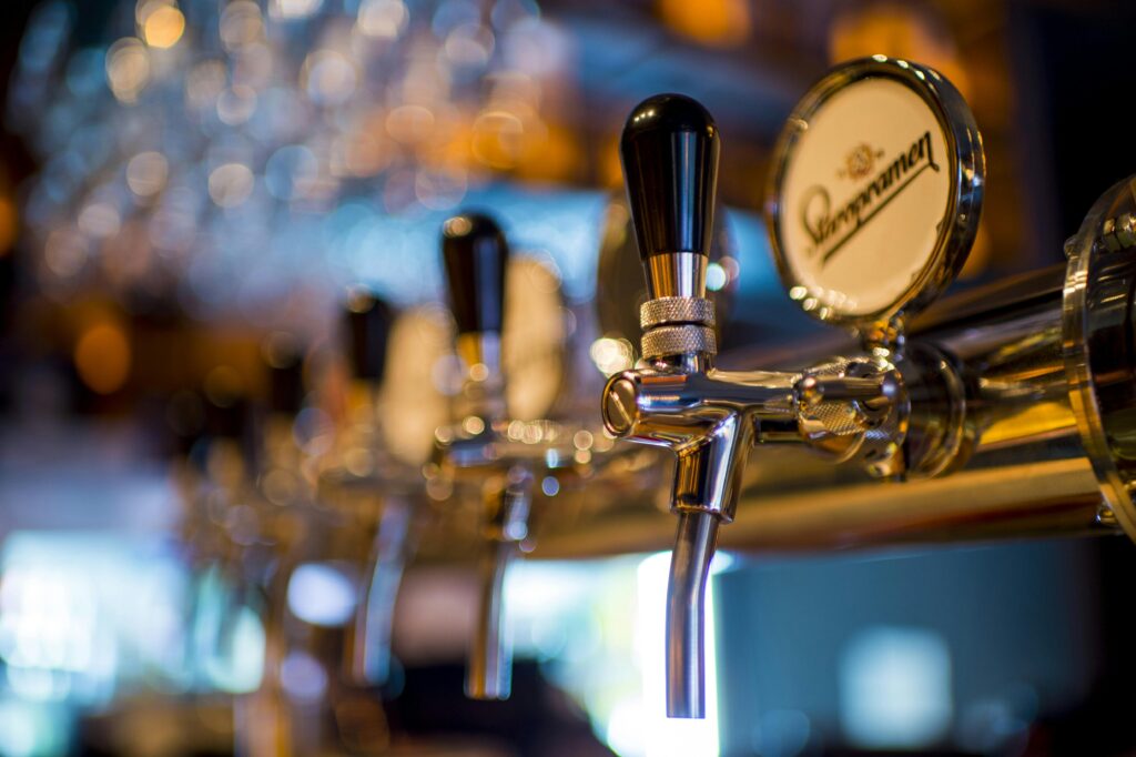 Close-up of a beer tap at Hawkstone Brewery, surrounded by various beer bottles in a cozy taproom setting.