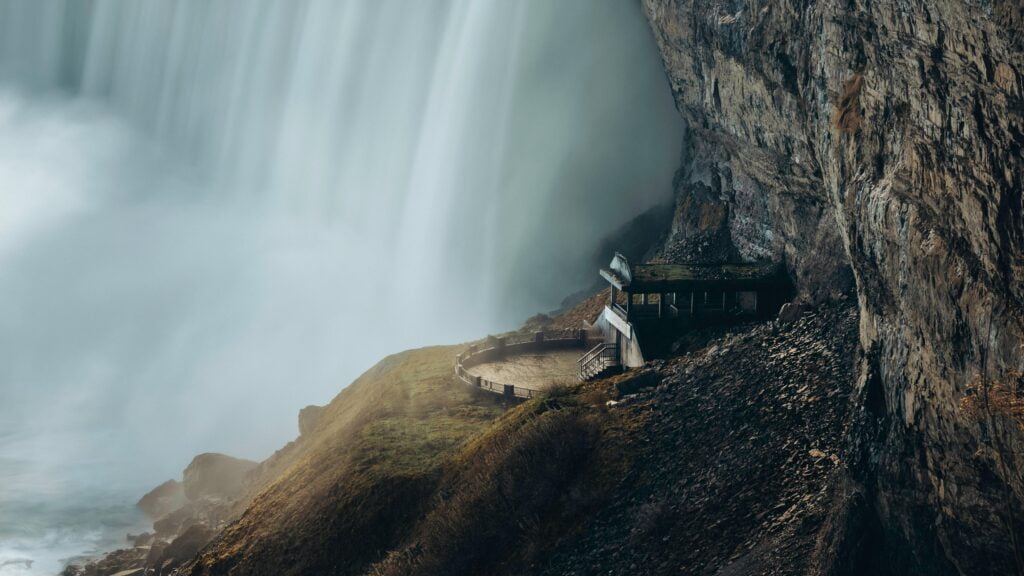 A quaint house perched on a cliffside, overlooking a stunning waterfall at Niagara Falls, inviting adventure and tranquility.